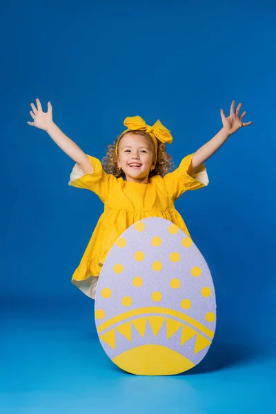 Счастливая Девушка Жёлтом Платье Большими Декоративными Пасхальными Яйцами Синем Фоне — стоковое фото