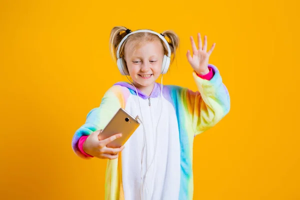 Szczęśliwa Dziewczynka Kigurumi Jednorożca Słucha Muzyki Słuchawkach Smartfona Izolacja Żółtym — Zdjęcie stockowe