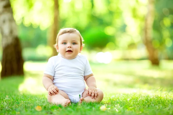 かわいいと幸せな幼児男の子でホワイトボディスーツ座っています上の緑の夏の草 — ストック写真