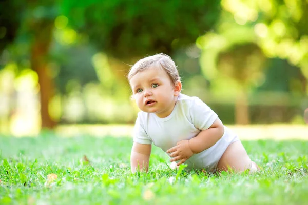 穿着白色紧身衣的可爱而快乐的幼儿坐在绿色的夏草上 — 图库照片