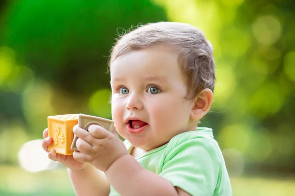 夏に芝生の上に座ってランナーキューブのおもちゃで遊ぶ緑のボディスーツのかわいい子供 子供の発達は1年の概念まで — ストック写真