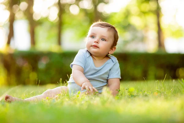 穿着白色紧身衣的可爱而快乐的幼儿坐在绿色的夏草上 — 图库照片