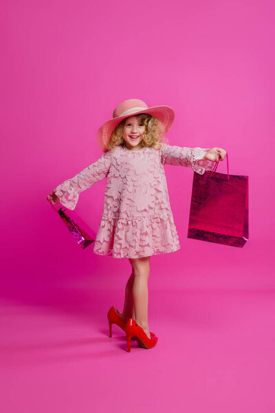 Little girl in her mother's big shoes, dress, hat and shopping bags. Little shopaholic. Copy space picture with placement for your text or advertisement