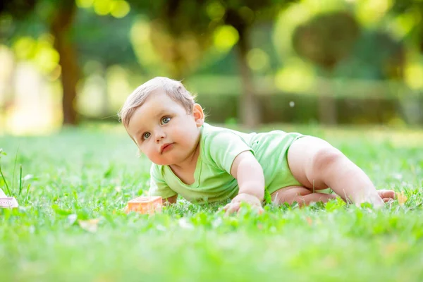 緑のボディスーツのかわいい幼児は夏に草の上を這います 赤ん坊は草の上を這うことを学ぶ — ストック写真