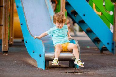 Neşeli kızıl saçlı çocuk renkli kaydırak ve çocuk parkına tırmanıyor.