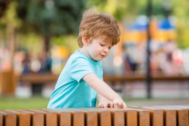 İki yıllık küçük çocuk yazın bir çocuk kasabasında ahşap bankta oynar. Çocuk yaşam tarzı konsepti