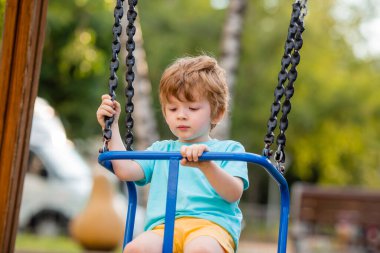 2 yıllık tatlı kızıl çocuk, çocuk parkında salıncakta sallanırken eğleniyor.