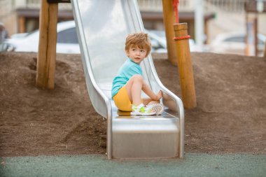 İki yıllık mavi tişörtlü kızıl saçlı sevimli çocuk oyun parkında kayarken eğleniyor. Çocuk yaşam tarzı konsepti
