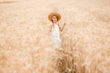 Hasır şapkalı sevimli küçük kız güneşli bir günde buğday tarlasında oynuyor.