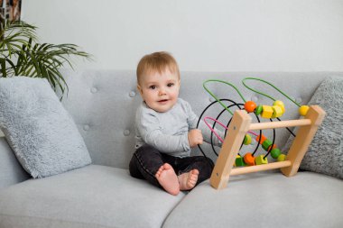 Küçük çocuk evdeki gri kanepede otururken gelişim oyunu oynuyor. 