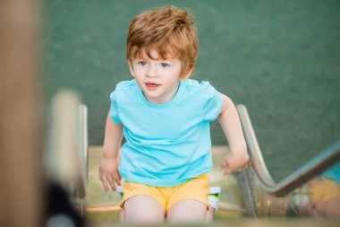 İki yıllık mavi tişörtlü kızıl saçlı sevimli çocuk oyun parkında kayarken eğleniyor. Çocuk yaşam tarzı konsepti