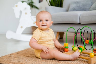 Sarı çizgili tulumlu şirin bebek halıda gelişim oyuncağıyla oynuyor. Çocuk gelişimi kavramı