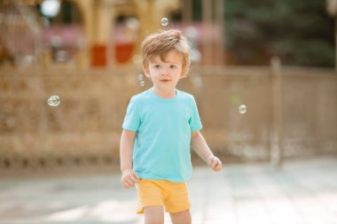 Mutlu kızıl çocuk, yaz eğlence parkında sabun köpüğüyle oynuyor. Çocuk yaşam tarzı ve mutluluk kavramı