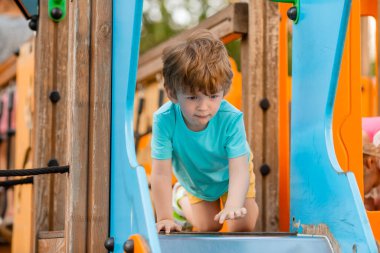 Neşeli kızıl saçlı çocuk renkli kaydırak ve çocuk parkına tırmanıyor.