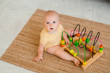 Sarı çizgili tulumlu şirin bebek halıda gelişim oyuncağıyla oynuyor. Çocuk gelişimi kavramı