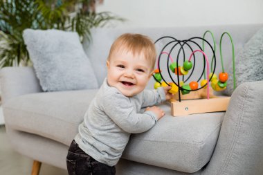 Küçük çocuk evdeki gri kanepede otururken gelişim oyunu oynuyor. 