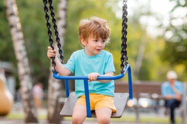 2 yıllık tatlı kızıl çocuk, çocuk parkında salıncakta sallanırken eğleniyor.