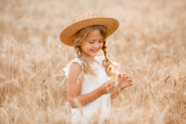 Hasır şapkalı sevimli küçük kız güneşli bir günde buğday tarlasında oynuyor.