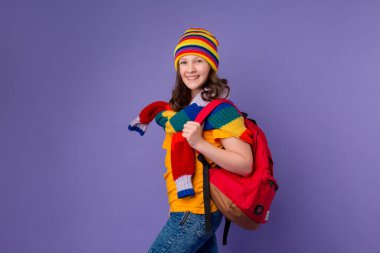 Sarı şapkalı liseli kız ve omzunda sırt çantası olan örgü ören süveter. Mor arka planda izole, gençlerin duygu konsepti..