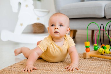 Sarı çizgili tulumlu şirin bebek halıda gelişim oyuncağıyla oynuyor. Çocuk gelişimi kavramı