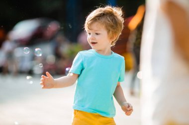 Mutlu kızıl çocuk, yaz eğlence parkında sabun köpüğüyle oynuyor. Çocuk yaşam tarzı ve mutluluk kavramı
