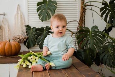 Ufaklık mutfakta masada oturuyor ve arkasında laleler ve canavarlar var.