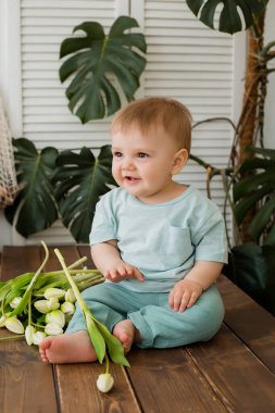 Ufaklık mutfakta masada oturuyor ve arkasında laleler ve canavarlar var.