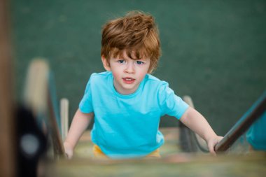 İki yıllık mavi tişörtlü kızıl saçlı sevimli çocuk oyun parkında kayarken eğleniyor. Çocuk yaşam tarzı konsepti