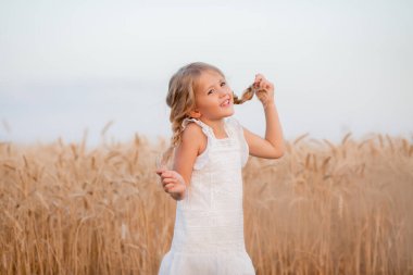 Saçları buğday tarlasında dikilen beyaz elbiseli sevimli bir kız. Doğal ve ekolojik yaşam konsepti