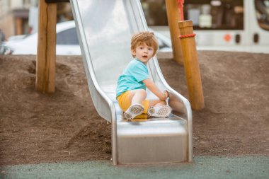 İki yıllık mavi tişörtlü kızıl saçlı sevimli çocuk oyun parkında kayarken eğleniyor. Çocuk yaşam tarzı konsepti
