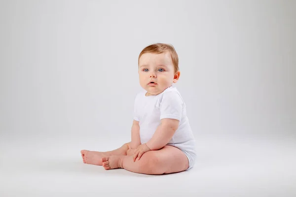 Cute toddler boy in white bodysuit sits still. Isolated image on white background