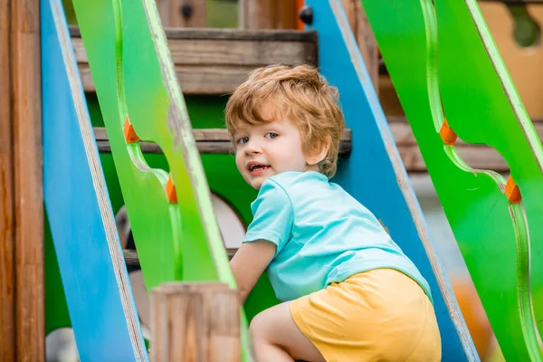 Neşeli kızıl saçlı çocuk renkli kaydırak ve çocuk parkına tırmanıyor.