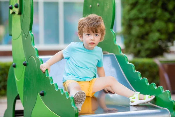 İki yıllık mavi tişörtlü kızıl saçlı sevimli çocuk oyun parkında kayarken eğleniyor. Çocuk yaşam tarzı konsepti