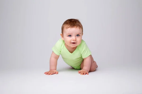 緑のボディスーツのかわいい幼児が床を這います 白い背景に孤立したイメージ — ストック写真