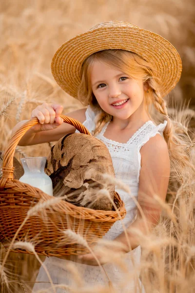 Buğday tarlasında elinde bir sepet ev ekmeği olan küçük sarışın bir kız. Çevre dostu eko tarım ürünleri kavramı.