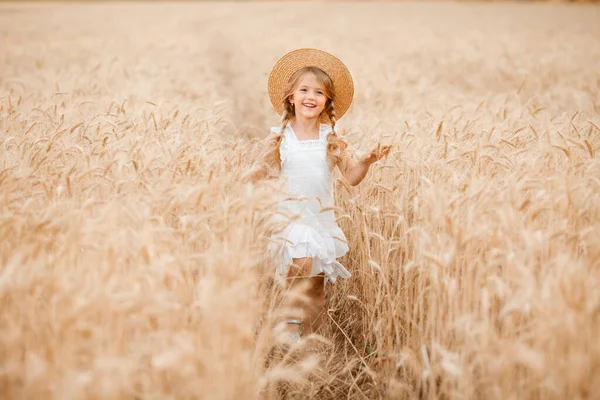 Hasır şapkalı sevimli küçük kız güneşli bir günde buğday tarlasında oynuyor.