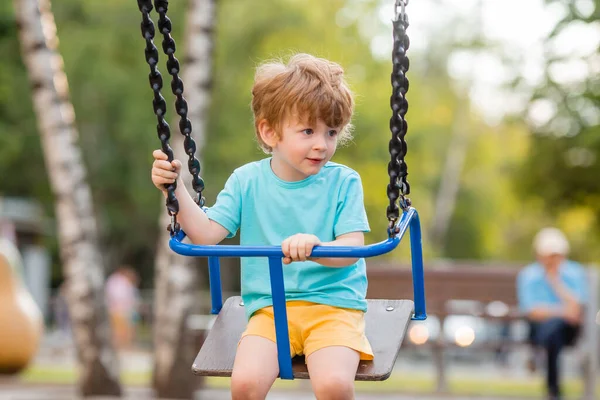 2 yıllık tatlı kızıl çocuk, çocuk parkında salıncakta sallanırken eğleniyor.