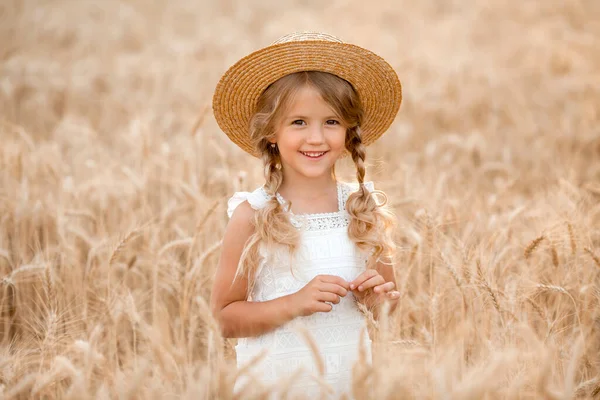 Hasır şapkalı sevimli küçük kız güneşli bir günde buğday tarlasında oynuyor.