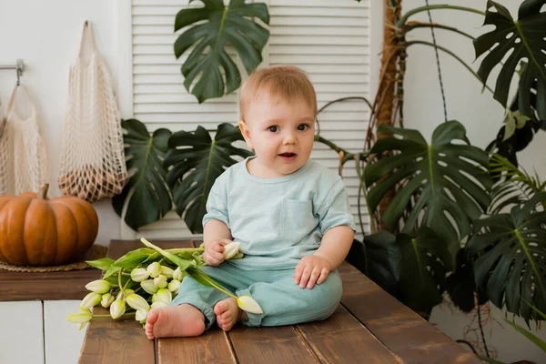 Ufaklık mutfakta masada oturuyor ve arkasında laleler ve canavarlar var.
