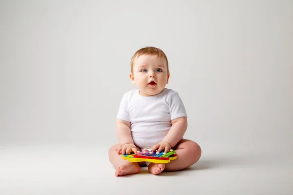Cute toddler boy in white bodysuit plays with developmental toy. Isolated image on white background
