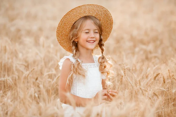 Hasır şapkalı sevimli küçük kız güneşli bir günde buğday tarlasında oynuyor.