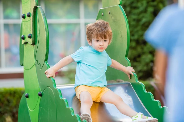 İki yıllık mavi tişörtlü kızıl saçlı sevimli çocuk oyun parkında kayarken eğleniyor. Çocuk yaşam tarzı konsepti