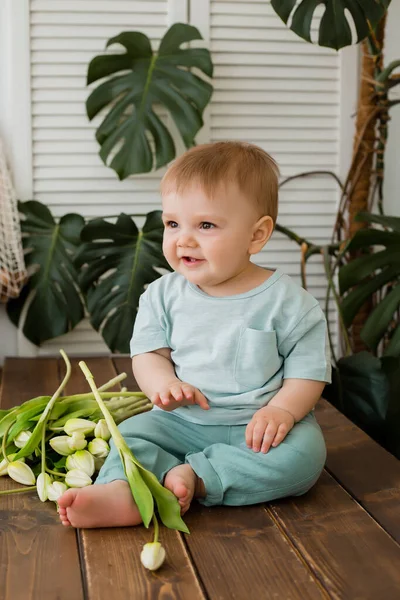 Ufaklık mutfakta masada oturuyor ve arkasında laleler ve canavarlar var.