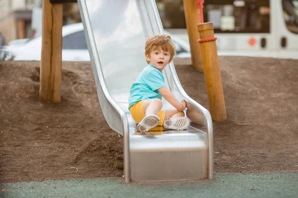 İki yıllık mavi tişörtlü kızıl saçlı sevimli çocuk oyun parkında kayarken eğleniyor. Çocuk yaşam tarzı konsepti