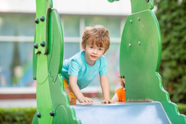 İki yıllık mavi tişörtlü kızıl saçlı sevimli çocuk oyun parkında kayarken eğleniyor. Çocuk yaşam tarzı konsepti