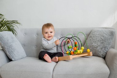 Küçük çocuk evdeki gri kanepede otururken gelişim oyunu oynuyor. 