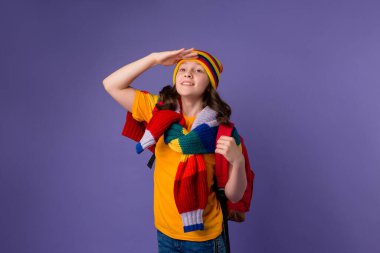 Sarı şapkalı liseli kız ve omzunda sırt çantası olan örgü ören süveter. Mor arka planda izole, gençlerin duygu konsepti..