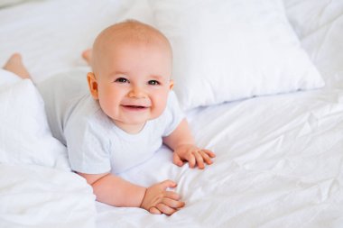 6 aylık neşeli bir erkek bebeğin beyaz bir bedenle yatakta fotoğrafı. 