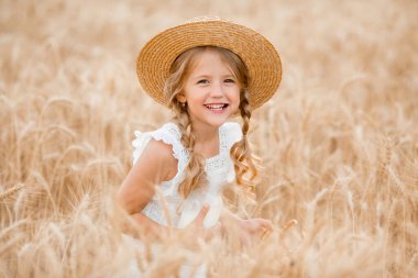Hasır şapkalı sevimli küçük kız güneşli bir günde buğday tarlasında oynuyor.