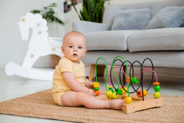 Sarı çizgili tulumlu şirin bebek halıda gelişim oyuncağıyla oynuyor. Çocuk gelişimi kavramı